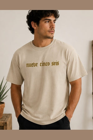 Man in profile wearing beige crew-neck tee with gold serif chest lettering